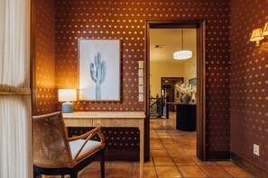 En hotellobby med ett konstverk föreställande en kaktus, en flätad fåtölj, en lampa och ett klinkergolv.