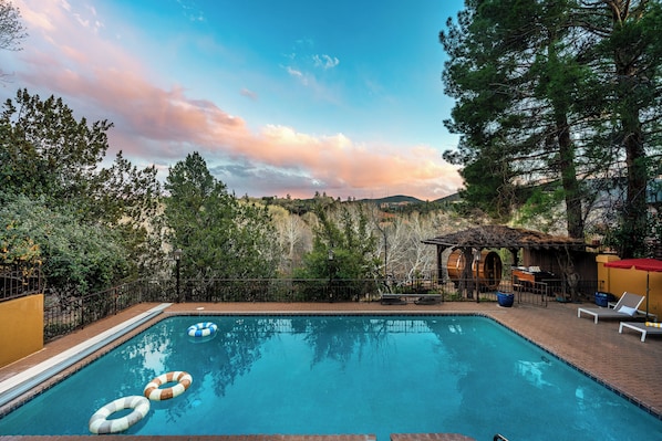 A swimming pool with lounge chairs and a rustic building in the background.