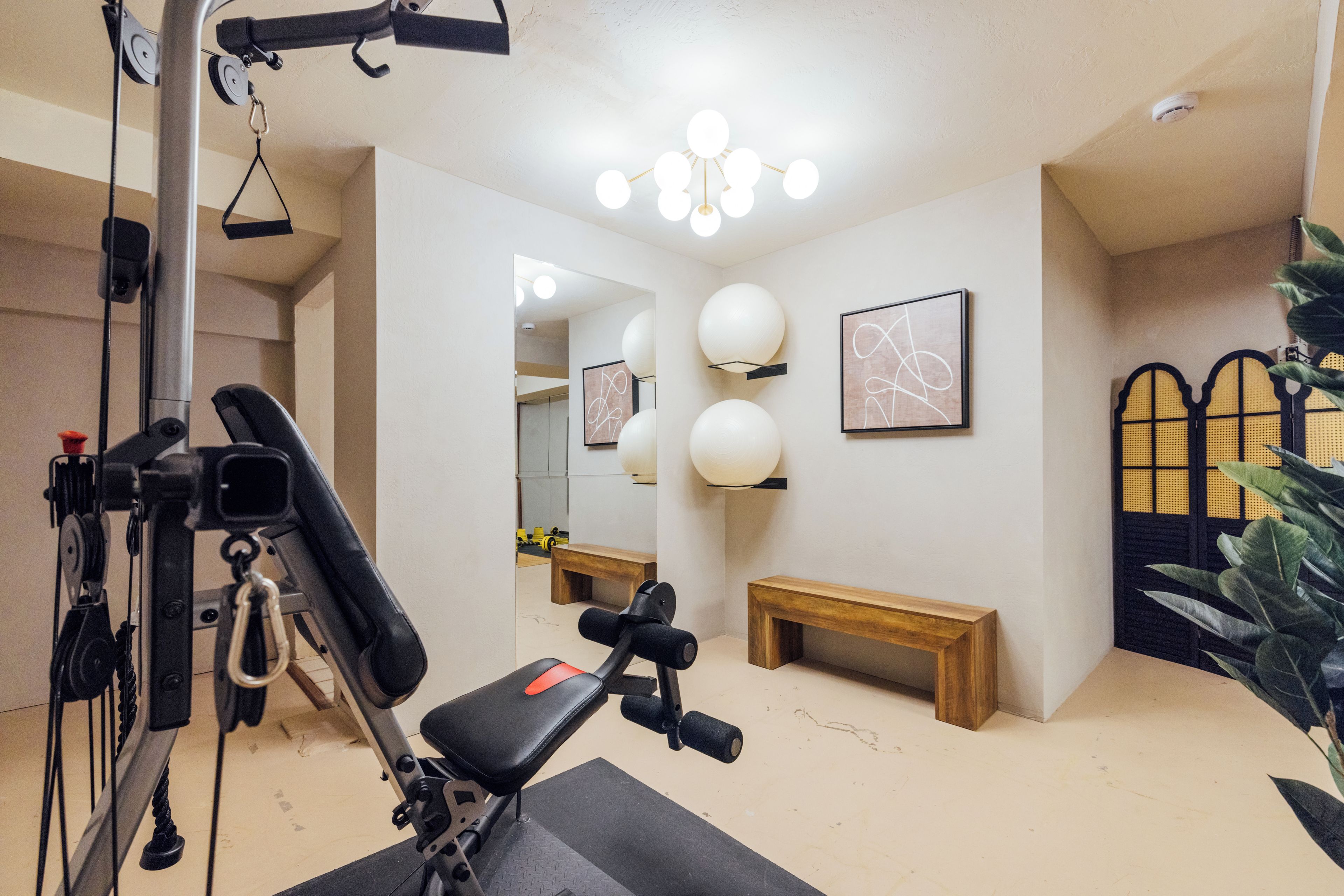 Une salle de sport équipée de matériel d’exercice, d’un banc et de lampes fixées au mur.