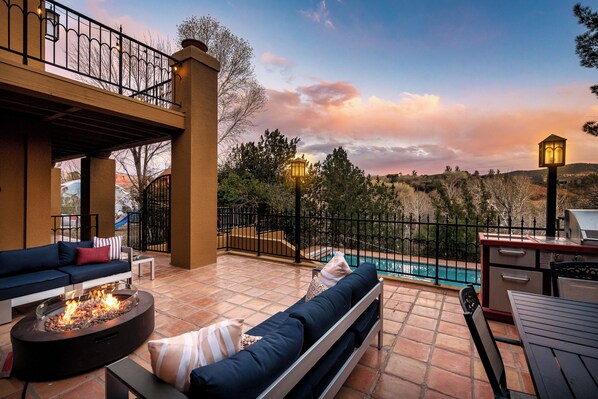 Un patio al aire libre con una chimenea, asientos y vista a una piscina.