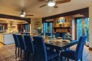 Uma sala de jantar com uma mesa grande, cadeiras estofadas em azul e um lustre.