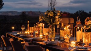 A table set for dining with candles, glasses, and a bottle, overlooking a mountainous landscape.