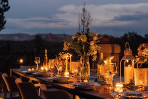A table set for dining with candles, glasses, and a bottle, overlooking a mountainous landscape.