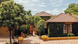 A courtyard with a paved walkway, a small building with a tiled roof, and a large tree.