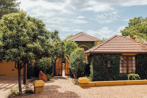 A courtyard with a paved walkway, a small building with a tiled roof, and a large tree.