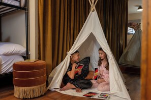 Una habitación con una cama litera, un reposapiés acolchado y una tienda tipi montada.