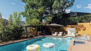 A swimming pool with two inflatable rings, surrounded by lounge chairs and a pergola.