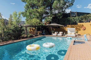 A swimming pool with two inflatable rings, surrounded by lounge chairs and a pergola.