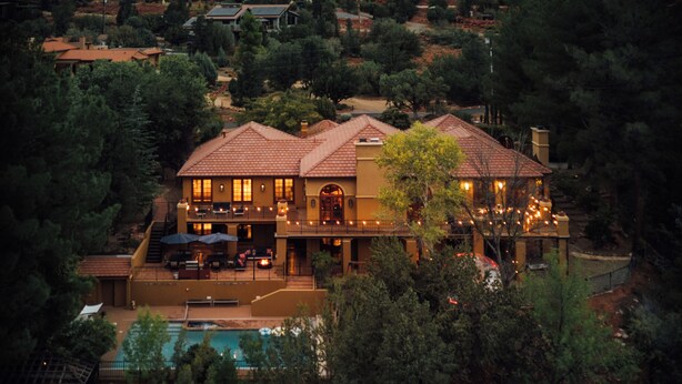 A large house with a pool, surrounded by trees and hills.
