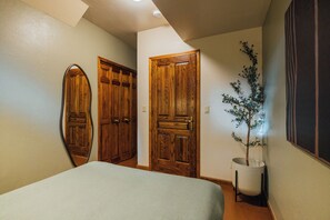 Une chambre à coucher avec un lit, deux portes en bois, une plante en pot et un miroir fixé au mur.