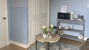 A room with a blue wall, a white door, a round table with plants, a coffee maker, and a microwave on a grey shelf. - Quiet Haven  (Freeport)
