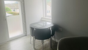 A small room with a round table and two chairs, a door leading outside, and a window with a view of houses. - Bike Park Cottage Sleeps 5 With Pet (Merthyr Tydfil)