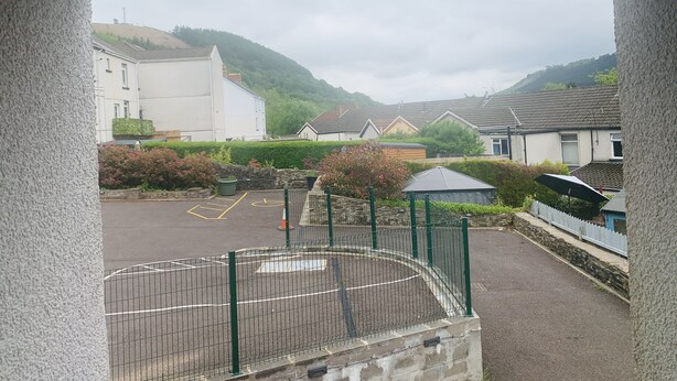 A view of a residential area with houses, a fenced playground, and a hill in the background. - Bike Park Cottage Sleeps 5 With Pet (Merthyr Tydfil)