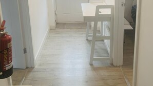A narrow hallway with a white door, a small table, and a chair. A fire extinguisher is mounted on the wall. - Bike Park Cottage Sleeps 5 With Pet (Merthyr Tydfil)