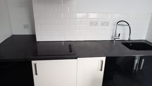 A kitchen with a black countertop, white cabinets, a stainless steel sink, and a white tiled backsplash. - Bike Park Cottage Sleeps 5 With Pet (Merthyr Tydfil)