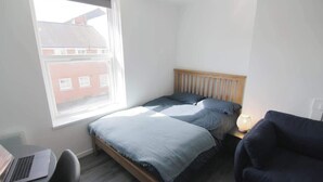 Ein Schlafzimmer mit einem Bett, einem Schreibtisch mit einem Laptop, einem Stuhl, einem Fenster und einer Lampe.