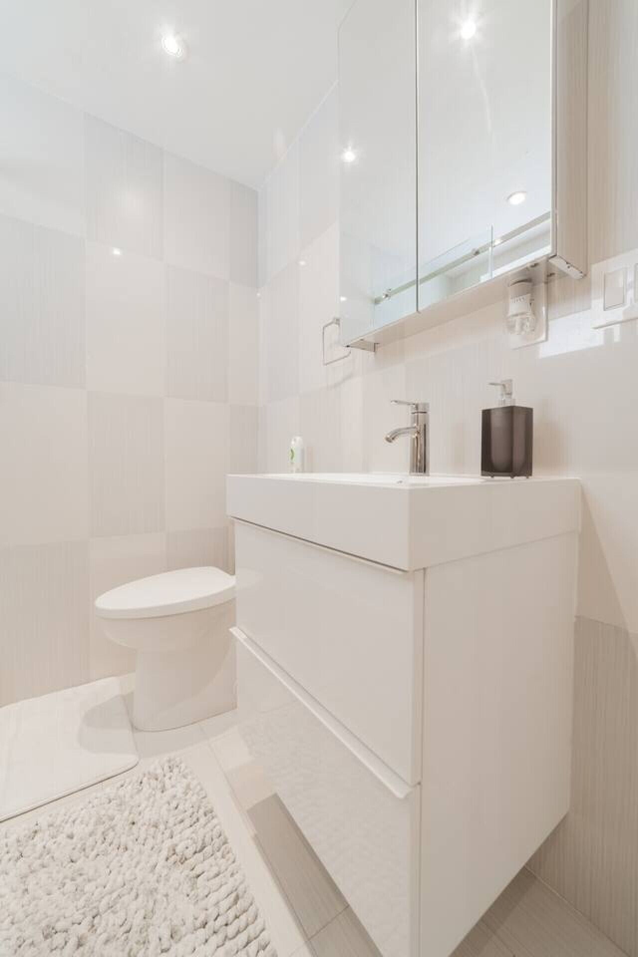 Un baño moderno con inodoro blanco, tocador con espejo y zona de ducha.