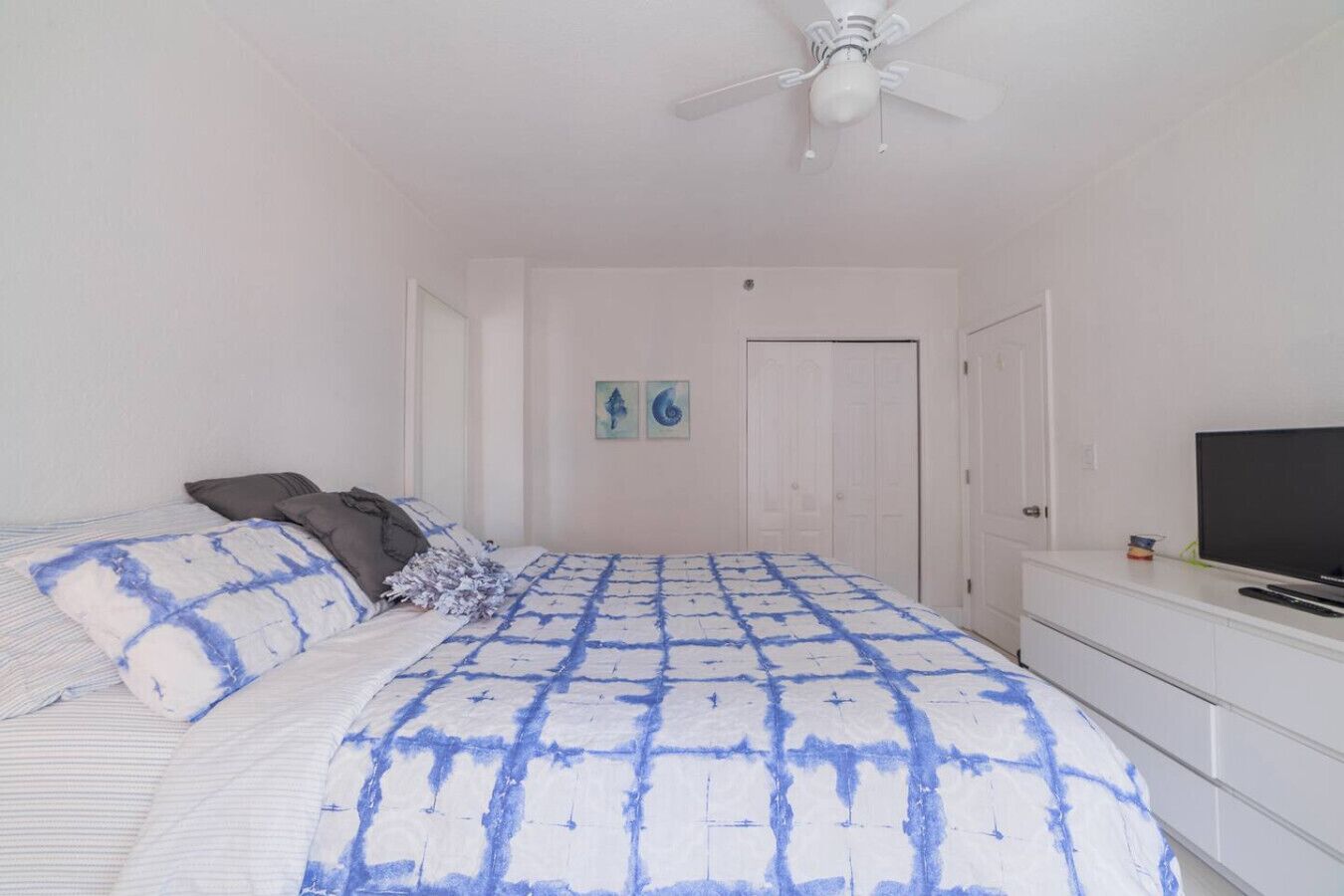 Un dormitorio con una cama, almohadas, un ventilador de techo, un televisor y un aparador.