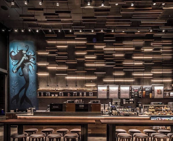 Een moderne bar met een lange toonbank, krukken en een menubord.