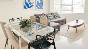 Un salon moderne avec une table à manger en verre, un canapé gris et deux tableaux abstraits accrochés au mur.