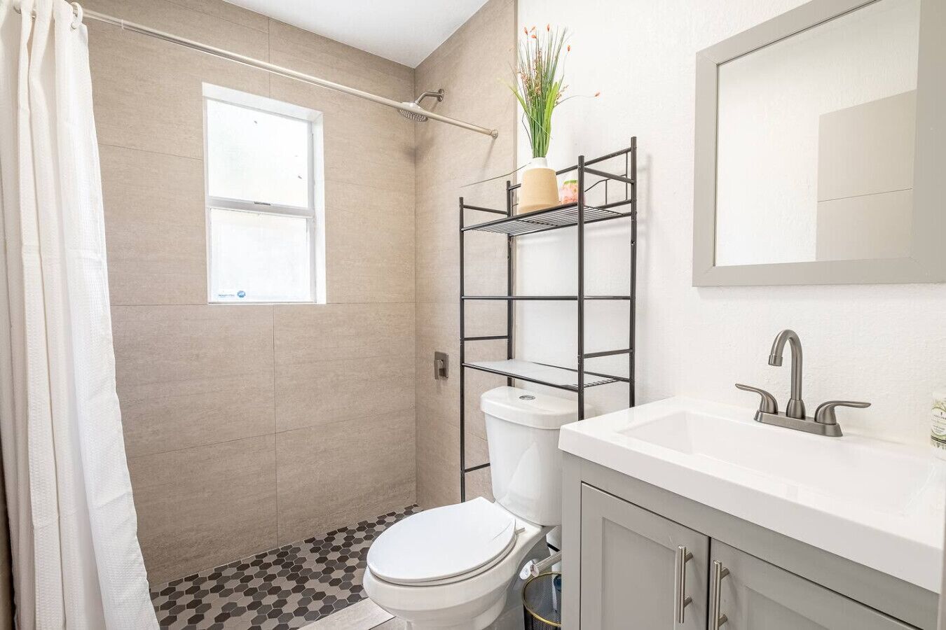 A bathroom with a toilet, sink, shower, and a shelf with plants.