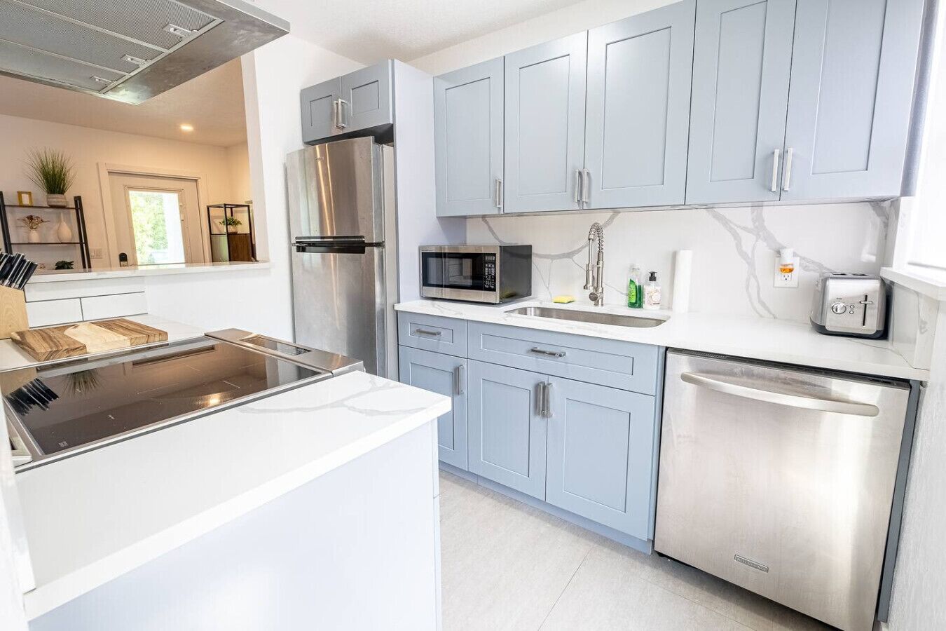 A modern kitchen with stainless steel appliances, light blue cabinets, and a white countertop.
