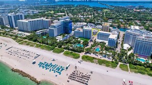 An aerial view of a coastal city with high-rise buildings, a beach with umbrellas, and a marina. - Newly remodeled apartment only 1 min to the beach! (Miami Beach)