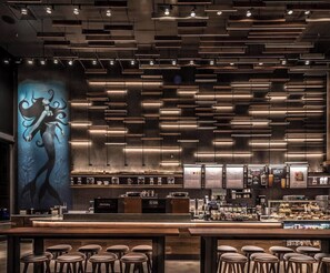 A modern bar with a long counter, stools, and a menu board.
