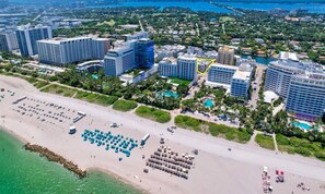 An aerial view of a coastal city with high-rise buildings, a beach with umbrellas, and a marina. - Newly remodeled apartment only 1 min to the beach! (Miami Beach)