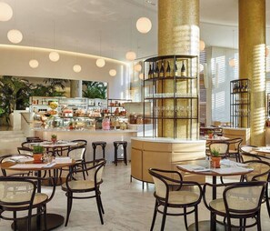 A spacious, well-lit hotel lobby with a central bar area, multiple seating arrangements, and a large decorative pillar.