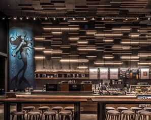 A modern Starbucks with a bar area, seating, and a mural on the wall.