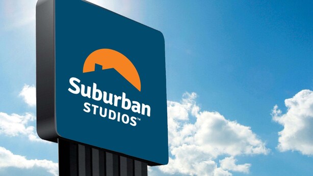 A sign for Suburban Studios with a clear blue sky and clouds in the background. - Suburban Studios McDonough South I-75 (McDonough)