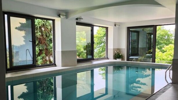 A modern indoor swimming pool with clear glass walls, large windows, and a tiled floor.