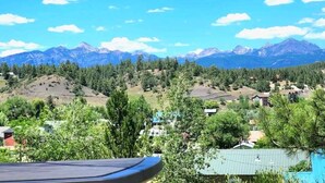 Une vue sur un paysage montagneux, avec un ciel dégagé, un pin et une maison avec un toit vert.