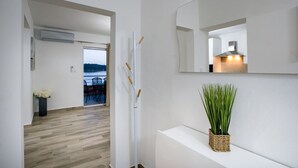 Un intérieur moderne avec un plancher en bois, une console blanche agrémentée d’une plante, un grand miroir et une vue sur un coin repas avec des chaises et une table.