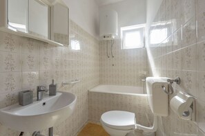 Bathroom features a sink, toilet, and shower area with a floral tile pattern and a window.