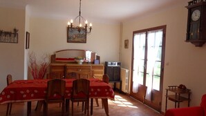 Un coin repas avec une table dressée pour quatre personnes, un lustre et un téléviseur en arrière-plan.