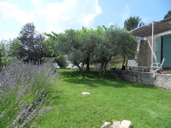 Un jardín con un muro de piedra, una pérgola y muebles de exterior.