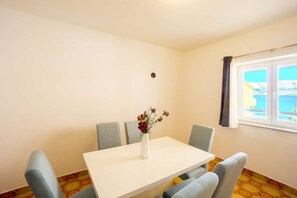 Enjoy a serene coastal retreat with a view of the sea from this stylish room, featuring a table and chairs, a vase with flowers, and a geometric-patterned floor.