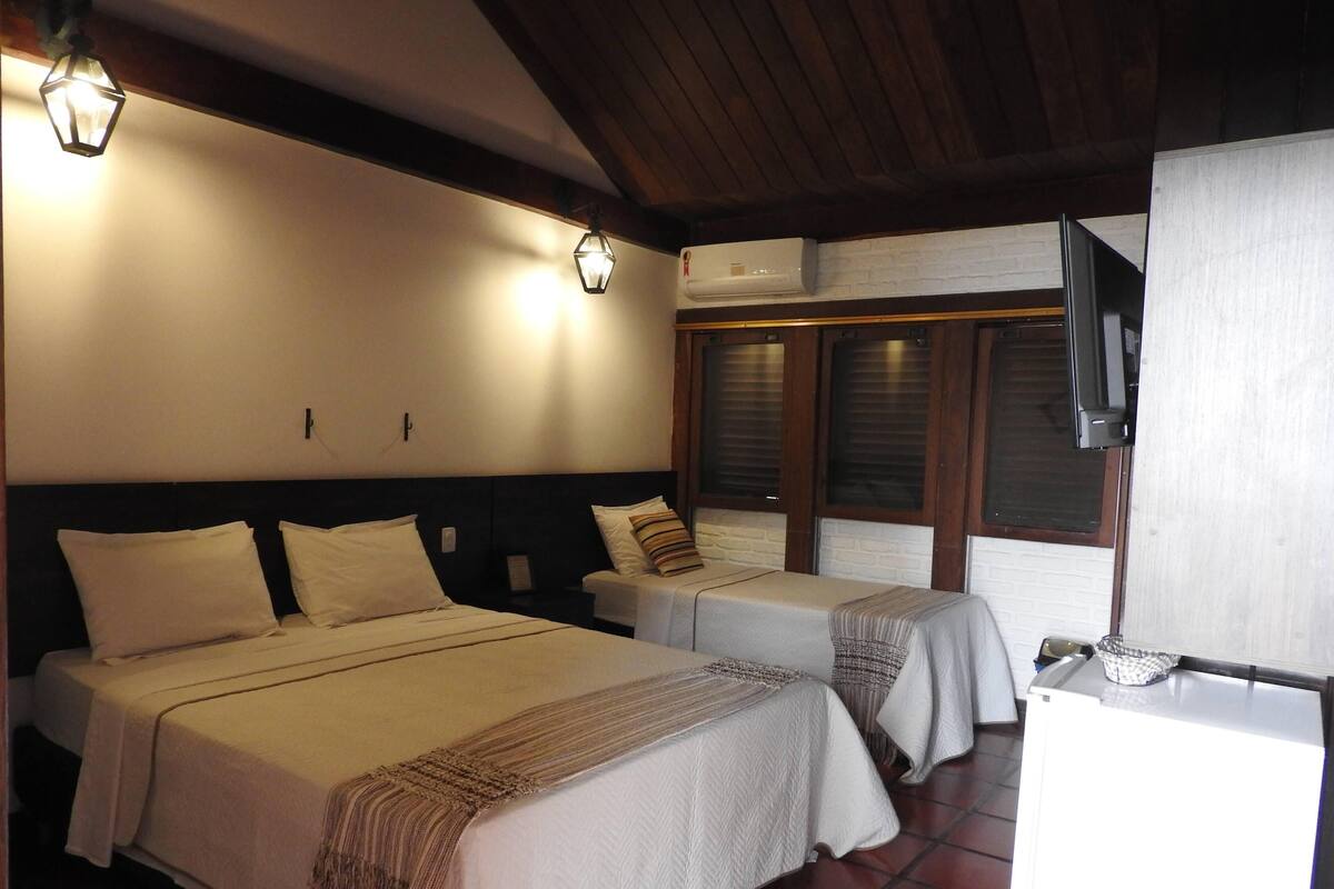 A hotel room with two beds, a TV, and an air conditioning unit.