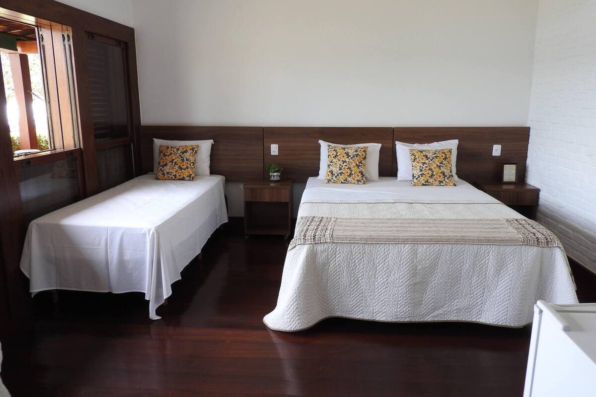 A hotel room with two single beds, wooden headboards, white bedding, and a small bedside table with a plant.