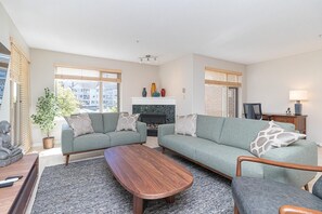 Ein modernes Wohnzimmer mit Kamin, zwei grünen Sofas, einem Holztisch und einer Topfpflanze.