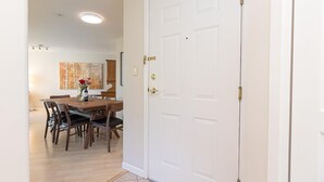 Ein Flur, der in einen Essbereich mit einem Holztisch und Stühlen führt, mit einer weißen Tür mit Messingklinke und einem Gemälde an der Wand.