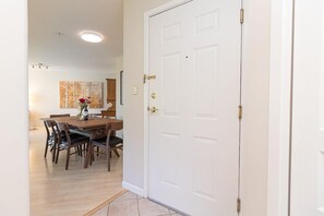 Ein Flur, der in einen Essbereich mit einem Holztisch und Stühlen führt, mit einer weißen Tür mit Messingklinke und einem Gemälde an der Wand.