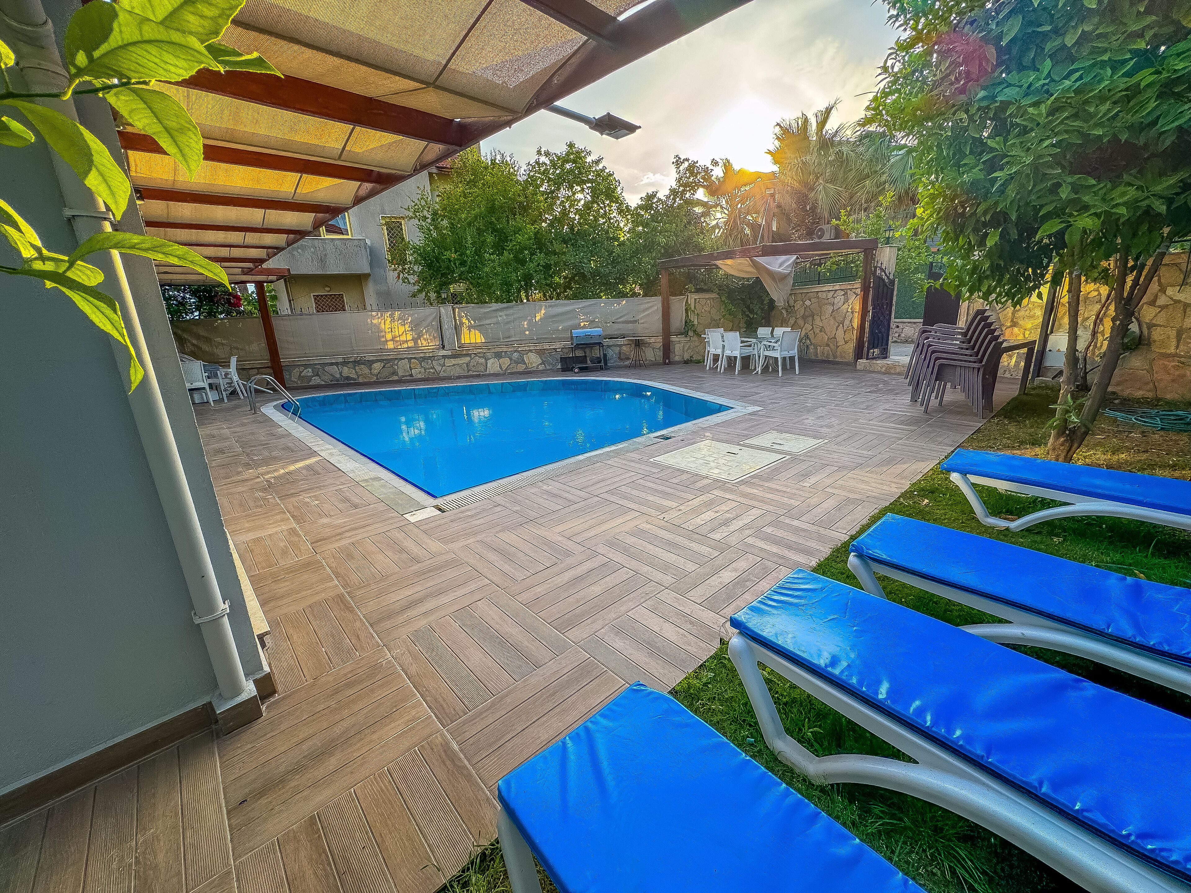 Una piscina con solárium, sillas de descanso y zona de estar techada.
