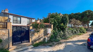 Una calle residencial con una entrada porticada, un muro de piedra y un coche estacionado.