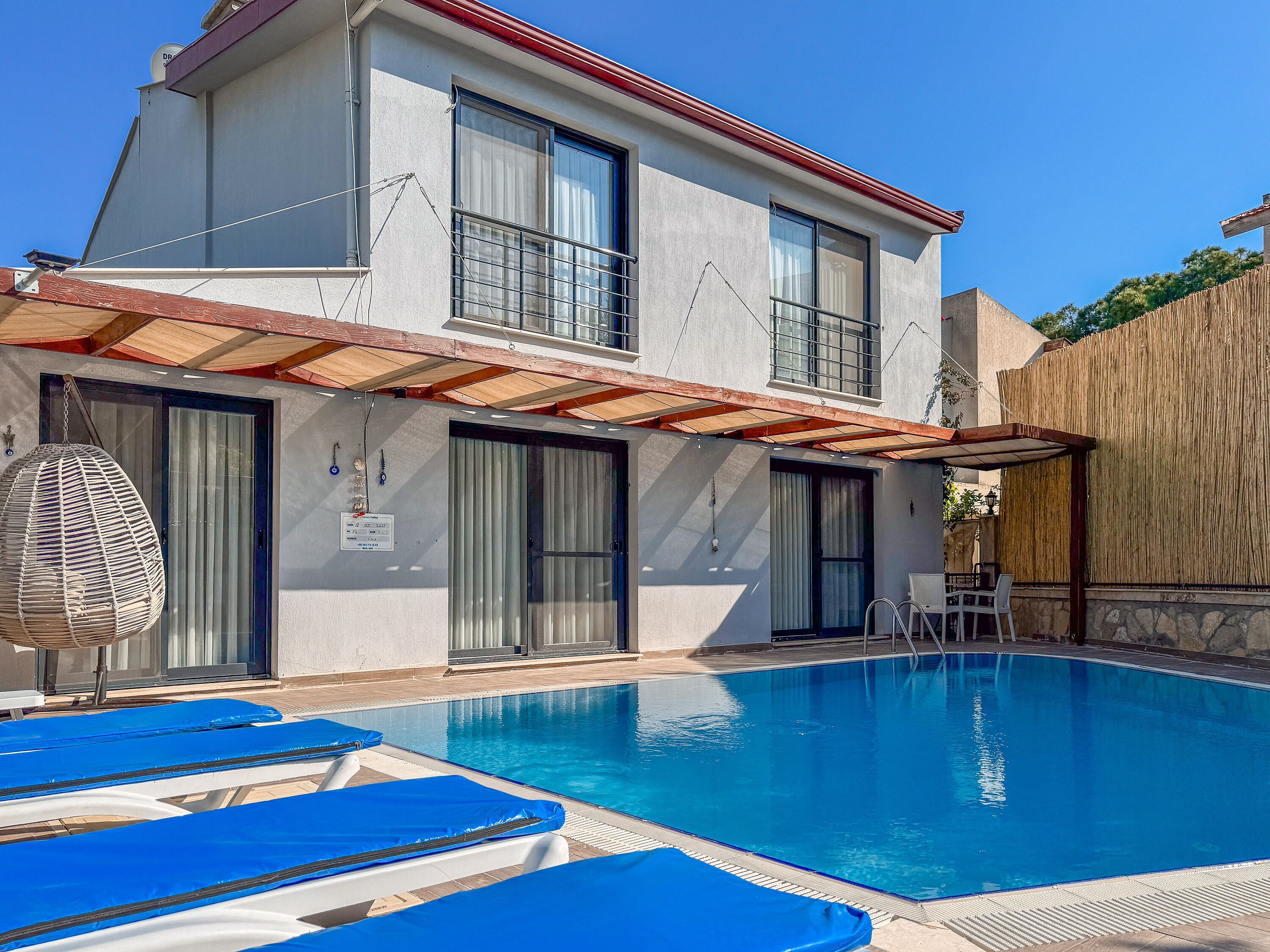 Un edificio de dos pisos con piscina, asientos al aire libre y un patio cubierto.