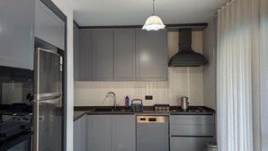 Una cocina moderna con armarios grises, un refrigerador de acero inoxidable, una estufa a gas y una lámpara colgante.