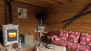 L’intérieur chaleureux d’un chalet avec un poêle à bois, un canapé rouge à motifs et une petite table agrémentée d’un élément décoratif.