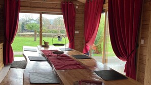 Un coin repas en bois avec une longue table, des rideaux rouges et une vue sur un jardin.